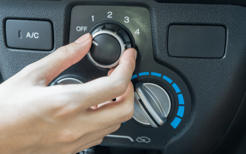 Person adjusts car climate control dial between 1 and 4 with blue temperature ring visible nearby